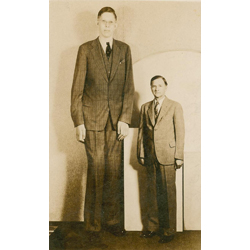 A photograph of Robert Wadlow, probably taken in the mid-1930’s. Robert was the world’s tallest man at 8 feet 11.1 inches (2.72 meters) in height. He is pictured next to his father, who is of average height.